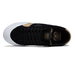 A black suede low-top skate shoe with a white rubber sole, gold logo detailing on the side and tongue, and a tan outsole edge, shown from a side profile view on a white background.