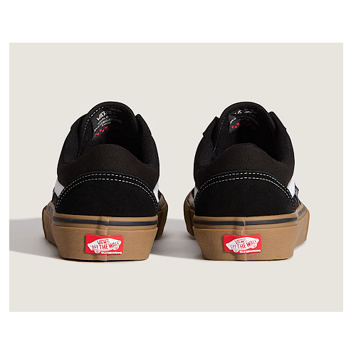 A pair of black Vans Old Skool sneakers shown from the back, featuring a brown gum sole and the signature red Vans logo on the heel.