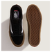 A pair of Vans Old Skool sneakers shown from the top and bottom, featuring a black suede and canvas upper with a white side stripe, black laces, and a brown gum sole. The bottom view shows the textured brown waffle-patterned outsole.